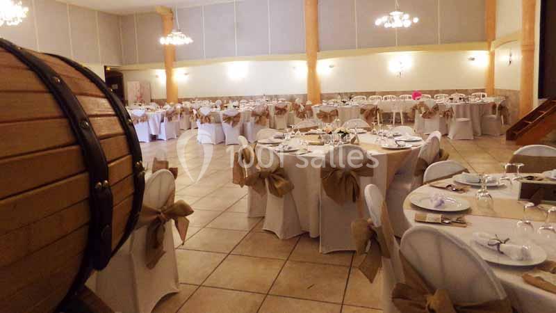 Salle de réception décorée avec des tables rondes dressées, nappes blanches et chaises ornées de nœuds beiges.