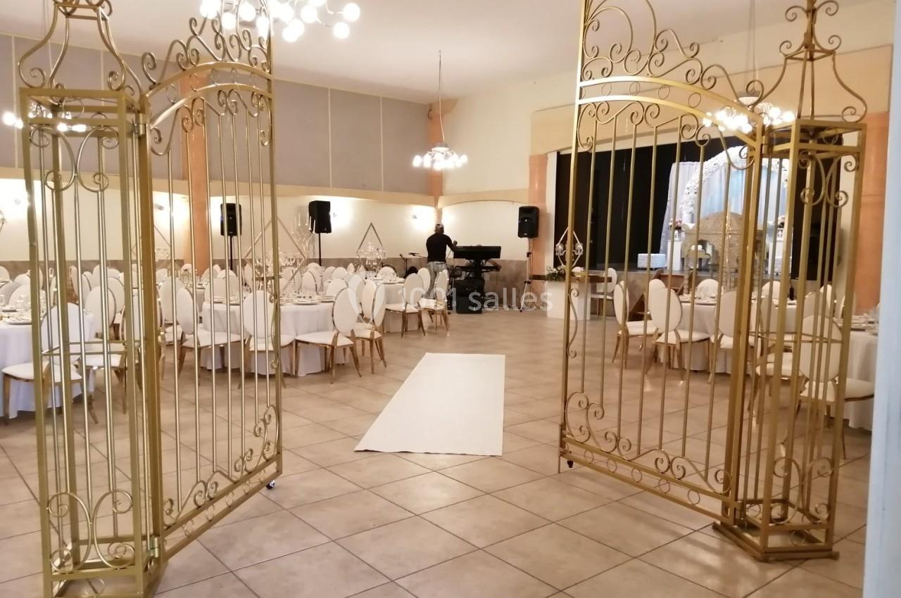 Salle de réception élégante avec tables dressées, décorations dorées et une arche métallique ouvrant sur un tapis blanc.