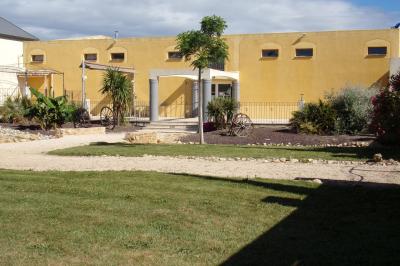 Cour extérieure avec végétation tropicale, terrasse ensoleillée, murs jaunes et mobilier en bois près d'une pergola.