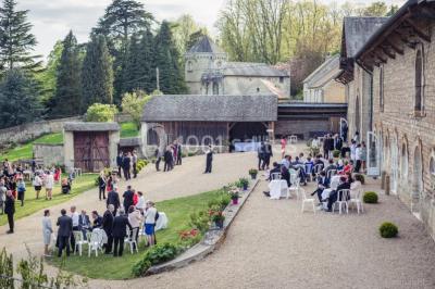 Vue depuis une arche en pierre sur une cour avec des fleurs en premier plan et un paysage champêtre en arrière-plan.