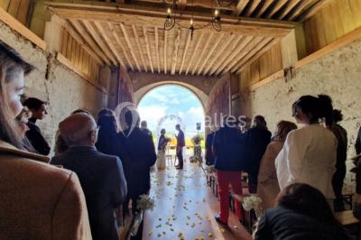 Vue depuis une arche en pierre sur une cour avec des fleurs en premier plan et un paysage champêtre en arrière-plan.