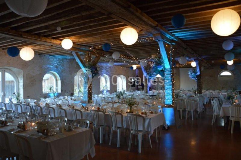 Salle de réception décorée avec des guirlandes lumineuses, des lanternes suspendues et des tables dressées pour un événement.