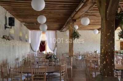Vue depuis une arche en pierre sur une cour avec des fleurs en premier plan et un paysage champêtre en arrière-plan.