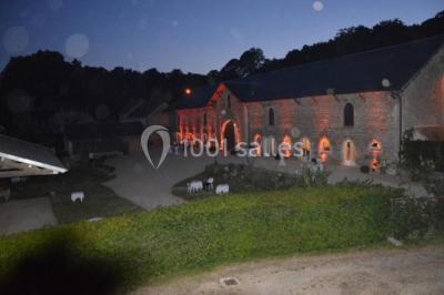 Vue depuis une arche en pierre sur une cour avec des fleurs en premier plan et un paysage champêtre en arrière-plan.