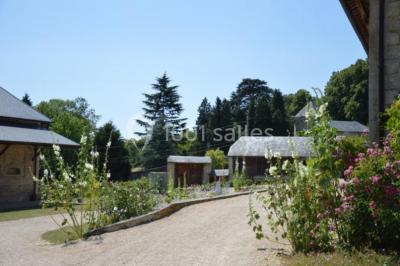 Vue depuis une arche en pierre sur une cour avec des fleurs en premier plan et un paysage champêtre en arrière-plan.