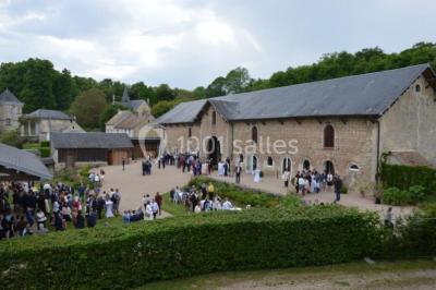 Vue depuis une arche en pierre sur une cour avec des fleurs en premier plan et un paysage champêtre en arrière-plan.