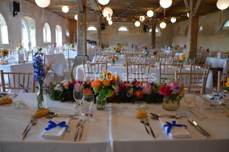 Salle de réception décorée pour un événement, avec tables dressées, fleurs colorées et chaises en bois clair.