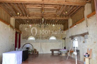 Vue depuis une arche en pierre sur une cour avec des fleurs en premier plan et un paysage champêtre en arrière-plan.