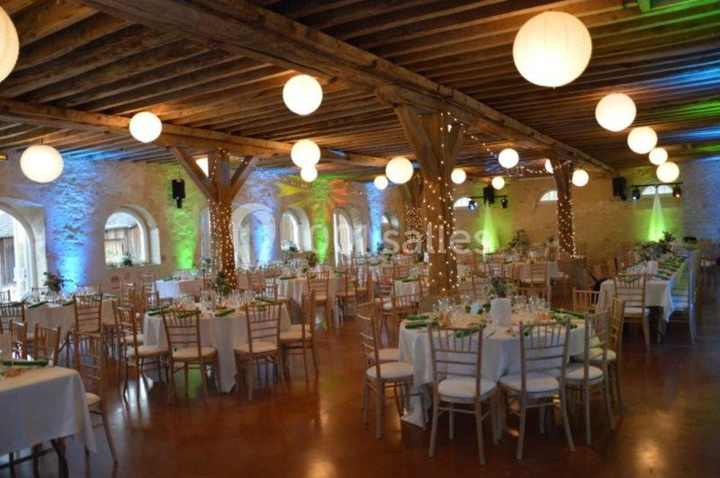 Salle de réception décorée avec des tables rondes, des chaises en bois, des guirlandes lumineuses et des lanternes…