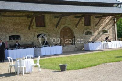 Vue depuis une arche en pierre sur une cour avec des fleurs en premier plan et un paysage champêtre en arrière-plan.