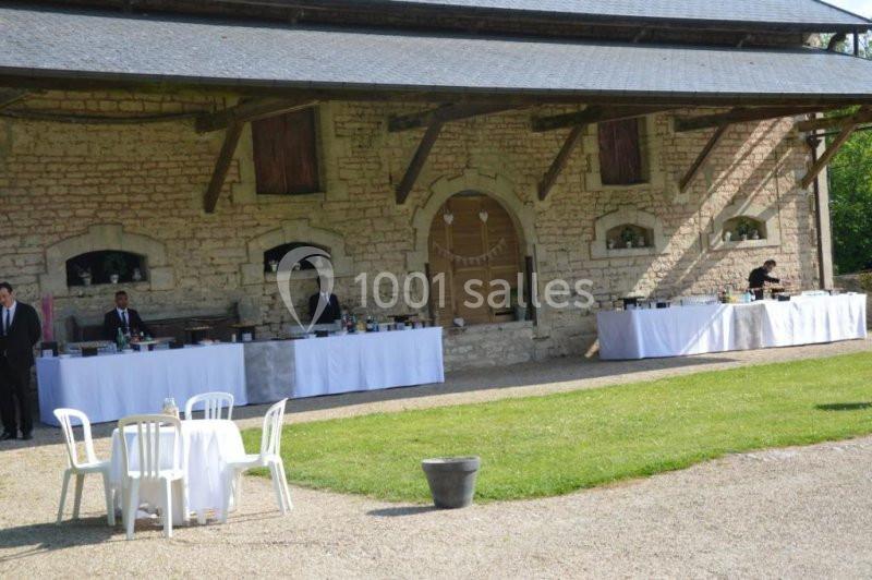 Tables de buffet dressées devant un bâtiment en pierre, avec des serveurs et des chaises blanches en extérieur.