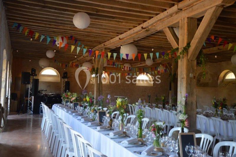 Salle de réception décorée avec des guirlandes colorées, des tables dressées et des fleurs en centre de table.