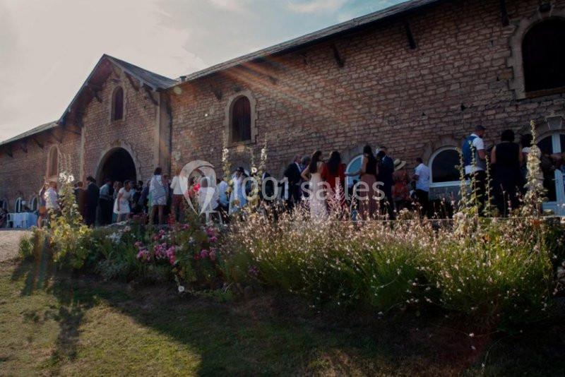 Groupe de personnes rassemblées devant un bâtiment en pierre, entouré de fleurs et baigné de lumière naturelle.