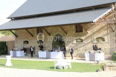Vue depuis une arche en pierre sur une cour avec des fleurs en premier plan et un paysage champêtre en arrière-plan.