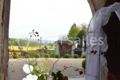 Vue depuis une arche en pierre sur une cour avec des fleurs en premier plan et un paysage champêtre en arrière-plan.