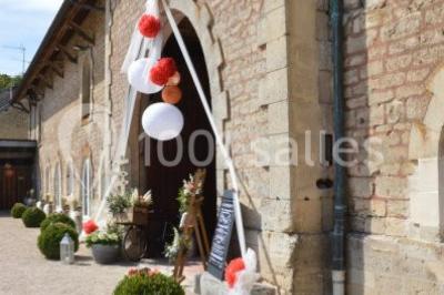 Vue depuis une arche en pierre sur une cour avec des fleurs en premier plan et un paysage champêtre en arrière-plan.