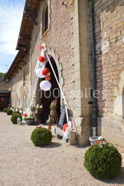 Entrée d'un bâtiment en pierre décorée pour un événement avec des lanternes, rubans et fleurs colorées.