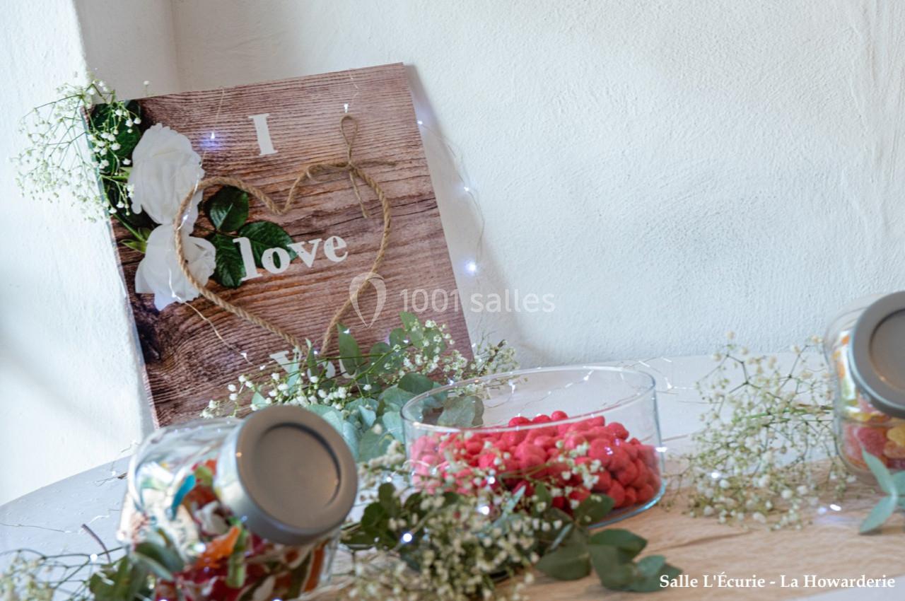 Décoration de table avec un panneau ’I love’ en bois, des bonbons dans des contenants et des fleurs blanches.