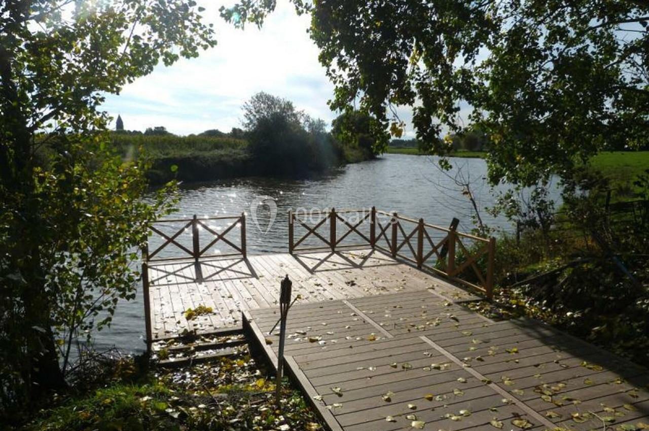 Ponton en bois bordé de barrières, donnant sur une rivière entourée de verdure et d'arbres sous une lumière naturelle.