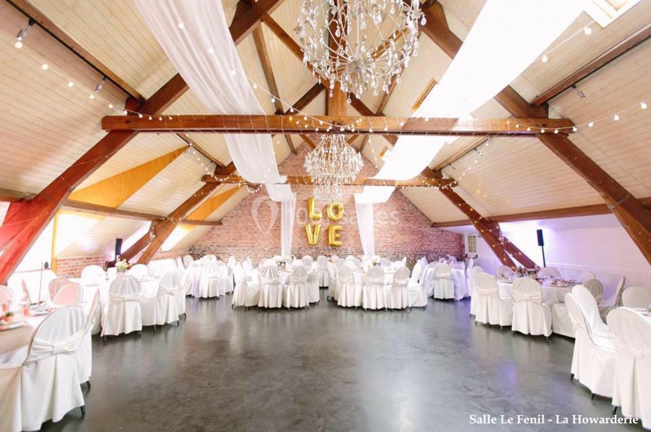 Salle de réception lumineuse avec poutres apparentes, tables rondes dressées et décoration ’LOVE’ en lettres dorées.
