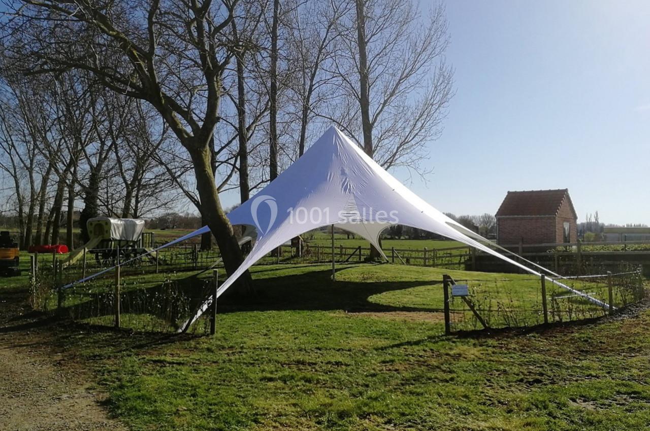Tente étoile blanche installée sur une pelouse entourée d'arbres et de clôtures dans un cadre rural.