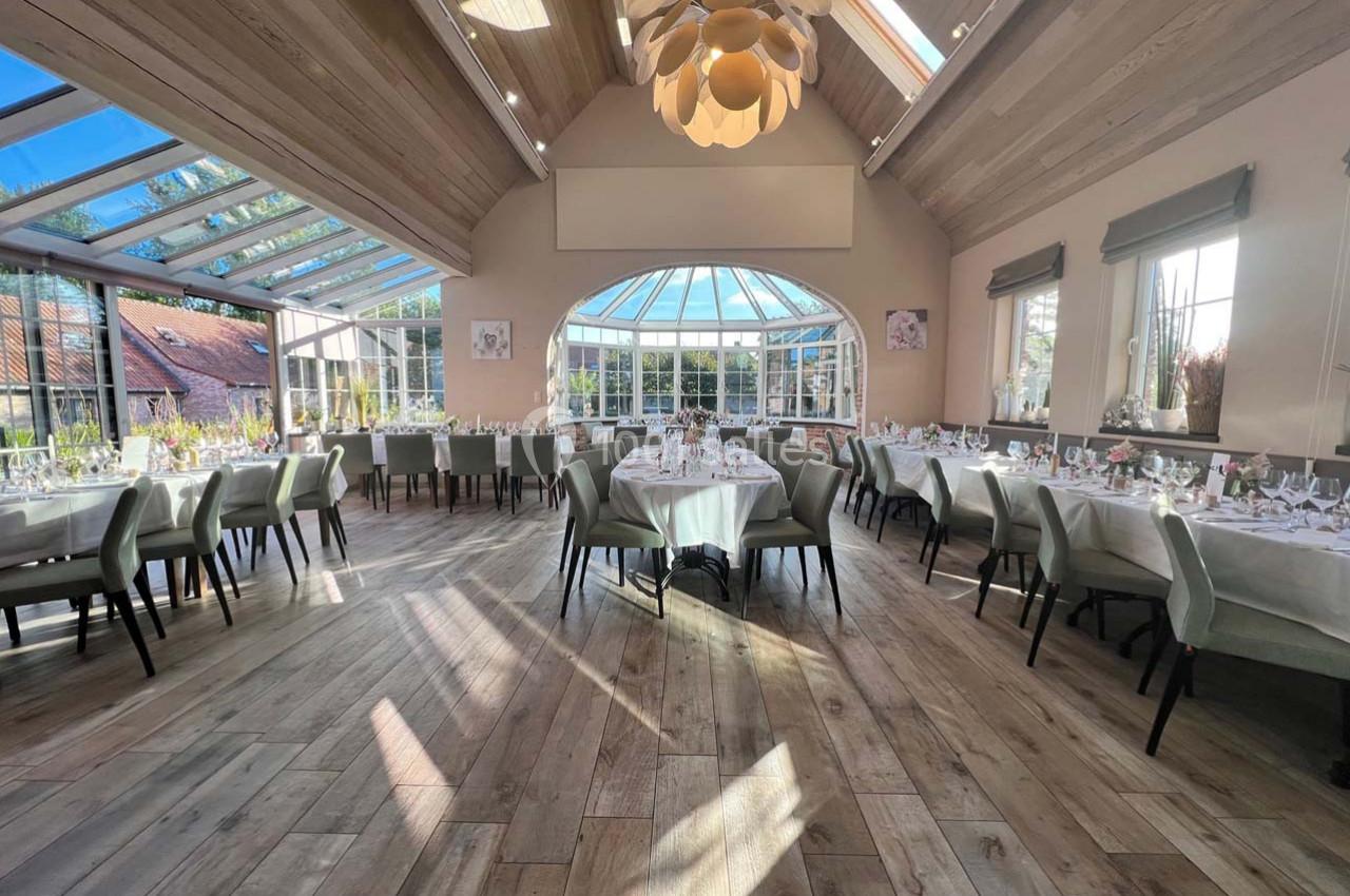 Salle de réception lumineuse avec tables dressées, grandes baies vitrées et plafond en bois clair.