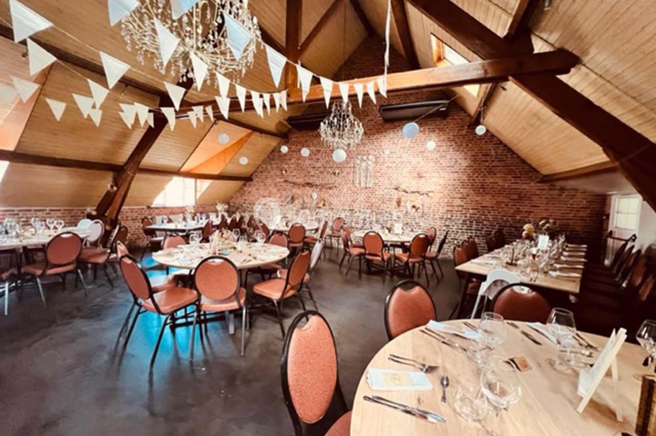 Salle de réception avec charpente apparente, tables dressées, guirlandes de fanions et décorations lumineuses suspendues.