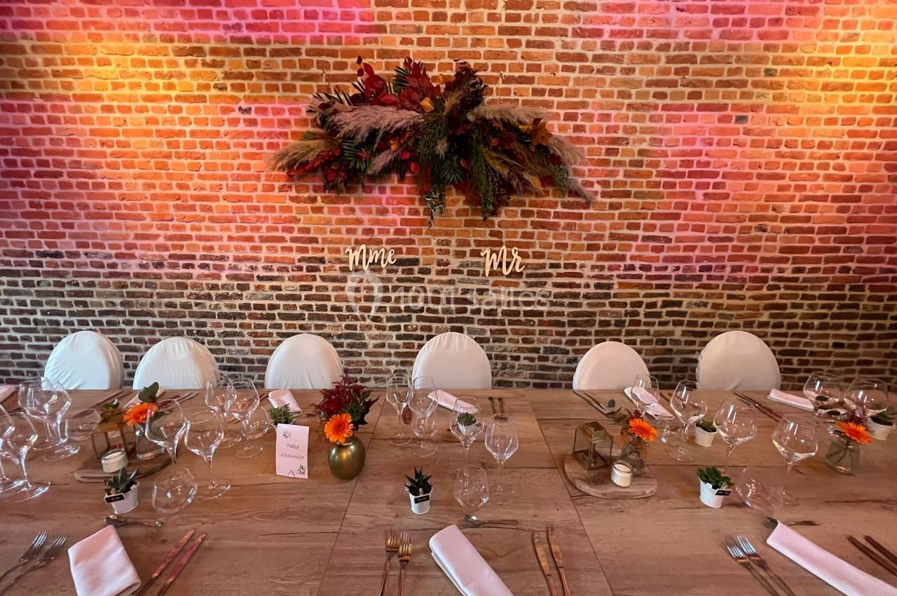 Table décorée pour un repas festif avec vaisselle élégante, fleurs colorées et mur de briques en arrière-plan.