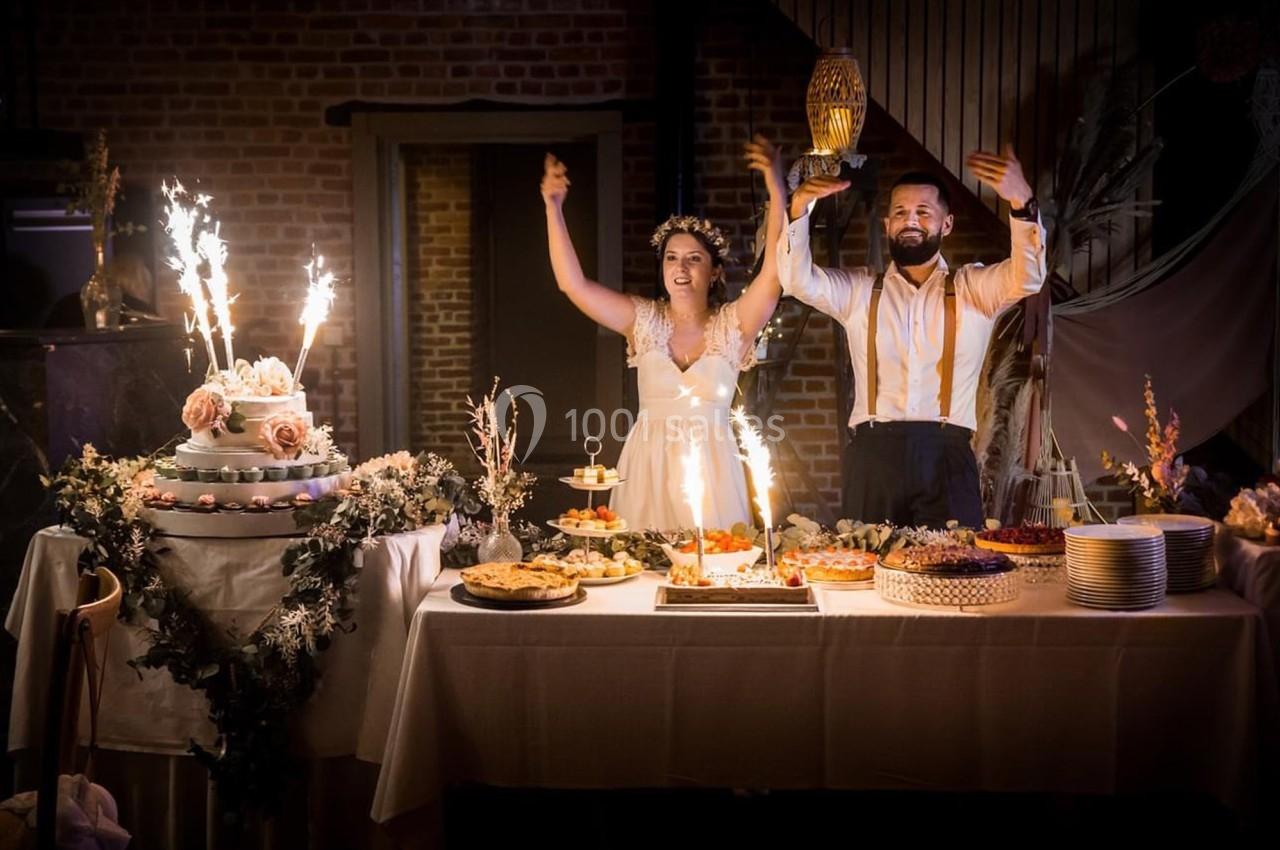 Un couple en tenue de mariage célèbre devant une table garnie de desserts et décorée avec des étincelles festives.
