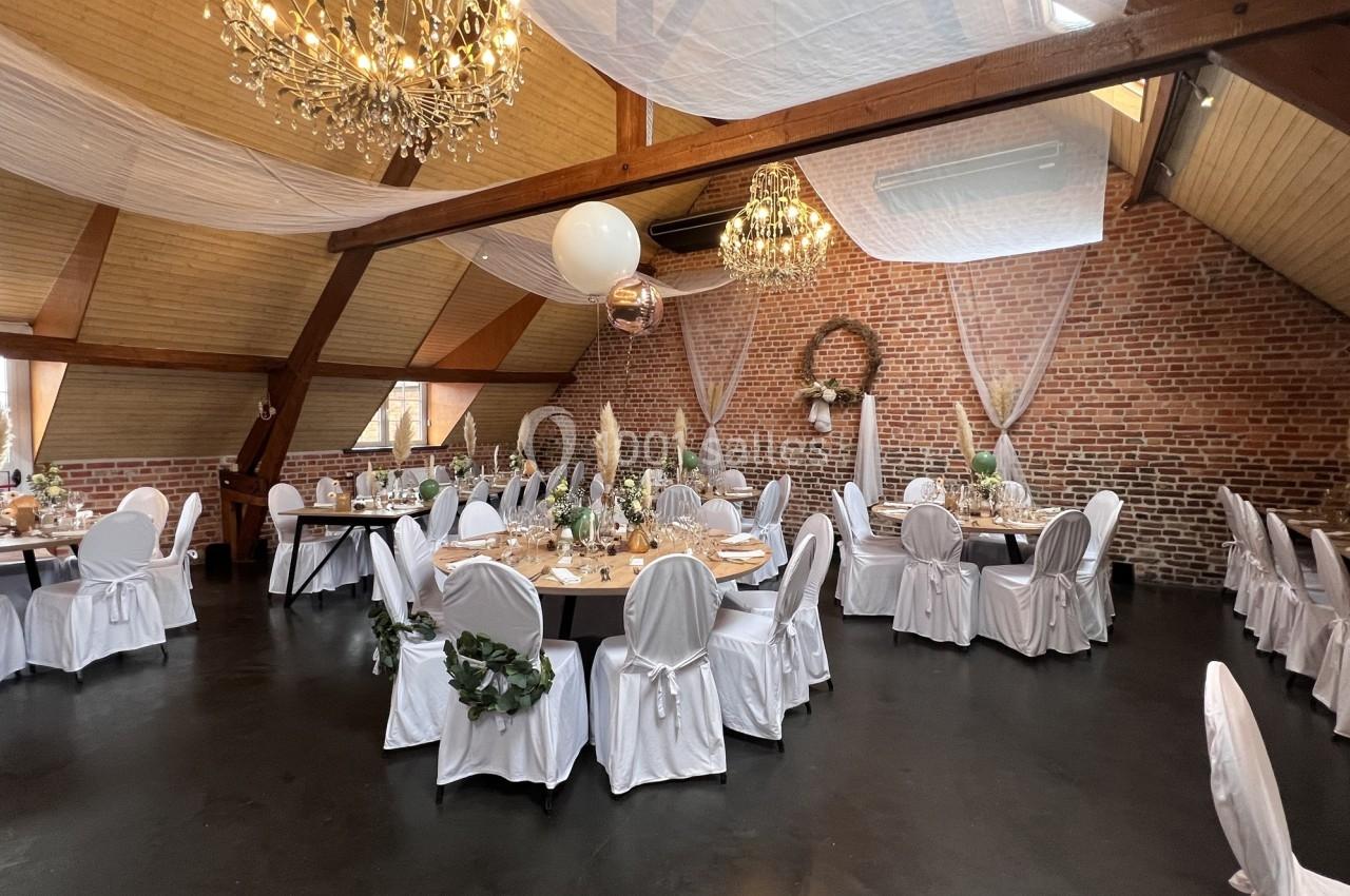 Salle de réception décorée pour un événement, avec chaises blanches, tables dressées et lustres suspendus.