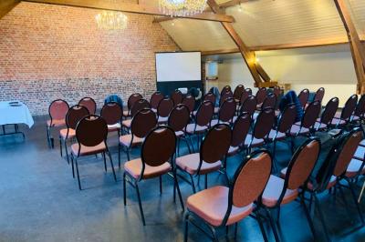 Salle de réunion avec des rangées de chaises face à un écran de projection, sous un plafond en briques apparentes.