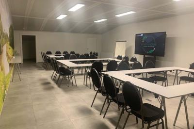 Salle de réunion avec des rangées de chaises face à un écran de projection, sous un plafond en briques apparentes.
