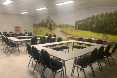 Salle de réunion avec des rangées de chaises face à un écran de projection, sous un plafond en briques apparentes.
