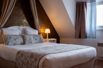 Chambre lumineuse avec lit double, murs à rayures roses, lampes de chevet et balcon donnant sur un paysage arboré.