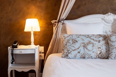 Chambre lumineuse avec lit double, murs à rayures roses, lampes de chevet et balcon donnant sur un paysage arboré.
