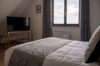 Chambre lumineuse avec lit double, murs à rayures roses, lampes de chevet et balcon donnant sur un paysage arboré.