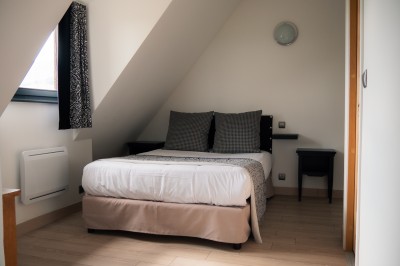 Chambre lumineuse avec lit double, murs à rayures roses, lampes de chevet et balcon donnant sur un paysage arboré.