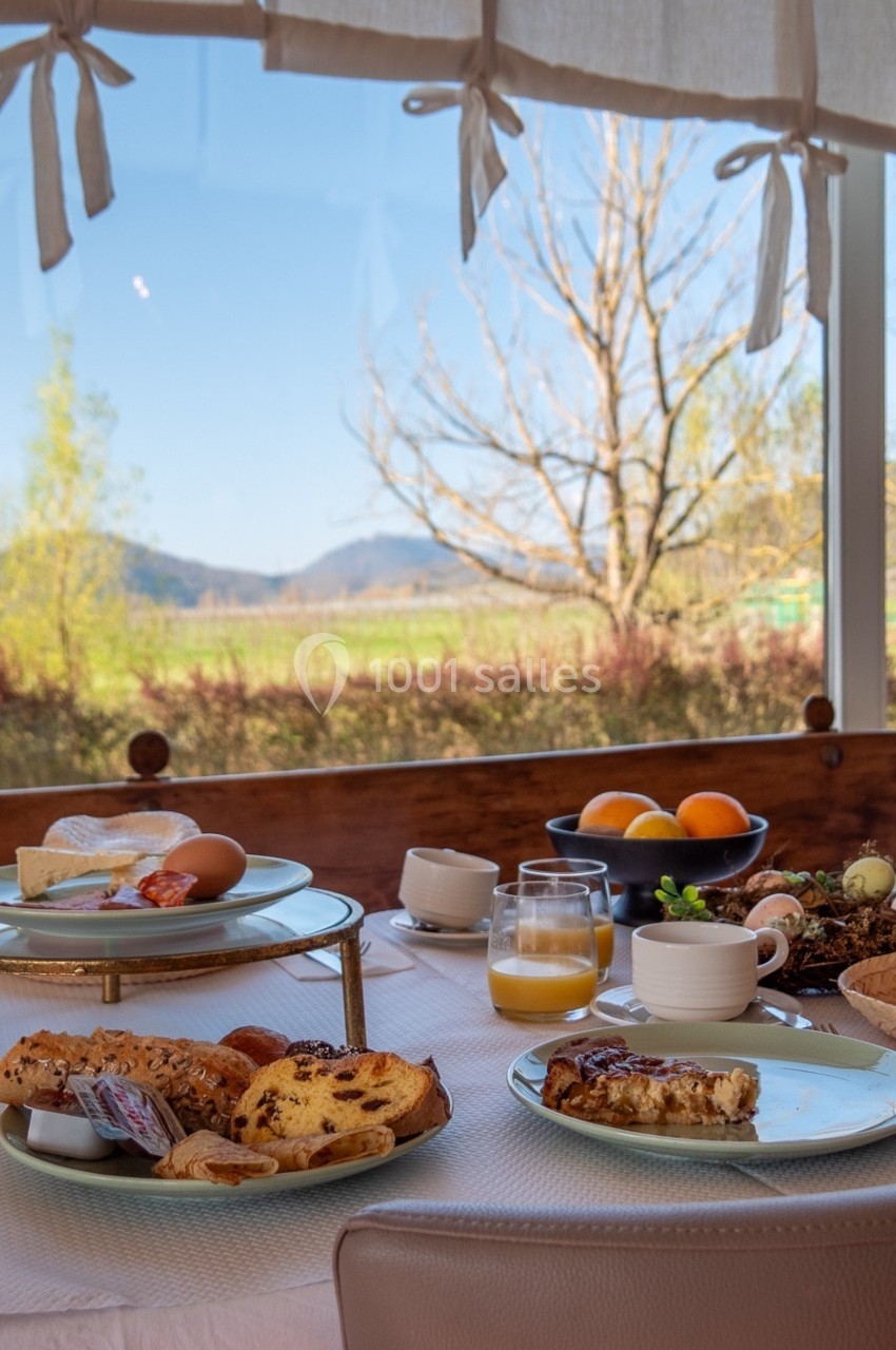 Petit-déjeuner servi sur une table près d'une fenêtre avec vue sur un paysage champêtre ensoleillé.
