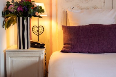 Table de chevet avec lampe allumée, vase de fleurs et téléphone, à côté d'un lit avec oreiller violet.