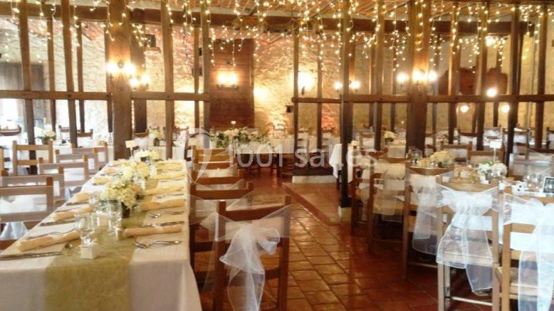 Salle de réception décorée avec des guirlandes lumineuses, tables dressées avec nappes blanches et arrangements floraux.
