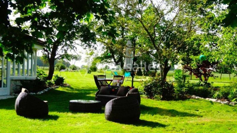 Mobilier de jardin en rotin disposé sur une pelouse verdoyante, entouré d'arbres et de végétation.