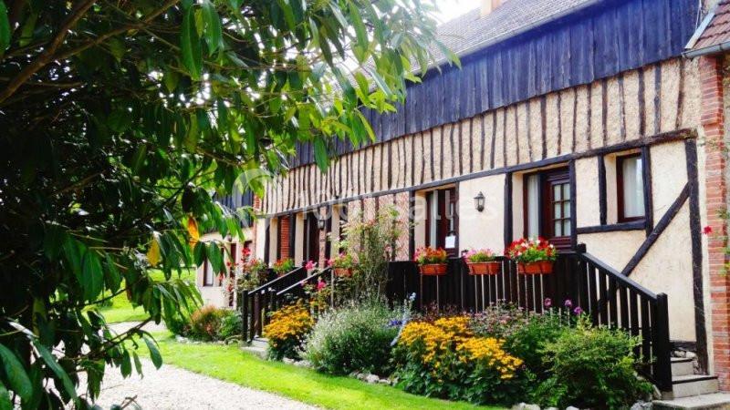 Façade d'une maison à colombages avec jardinières fleuries et parterre de fleurs, entourée de verdure.