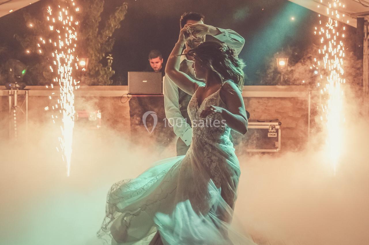 Un couple danse sous une tente décorée, entouré de fumée et d'effets lumineux avec des étincelles en arrière-plan.