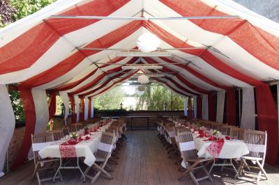 Tente rouge et blanche abritant des tables dressées avec nappes et décorations pour un repas en extérieur.