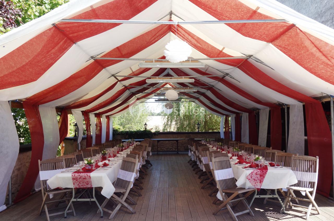 Tente rouge et blanche abritant des tables dressées avec nappes et décorations pour un repas en extérieur.