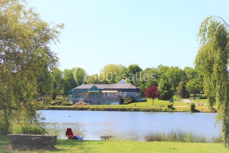 Vue d'un lac entouré de verdure avec un bâtiment en arrière-plan sous un ciel dégagé.