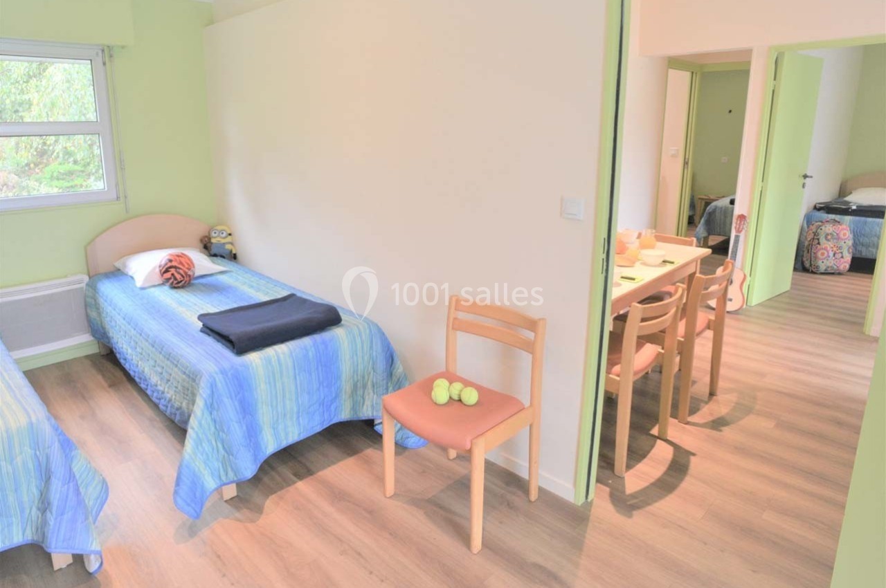 Location salle Merdrignac (Côtes-d'Armor) - Val de Landrouet #11 Deux lits simples avec couvre-lits bleus dans une chambre lumineuse, vue sur une salle à manger adjacente.