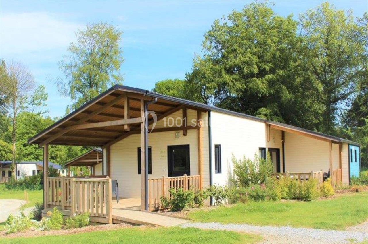 Location salle Merdrignac (Côtes-d'Armor) - Val de Landrouet #16 Chalet en bois clair avec terrasse couverte, entouré de verdure et situé dans un environnement arboré.
