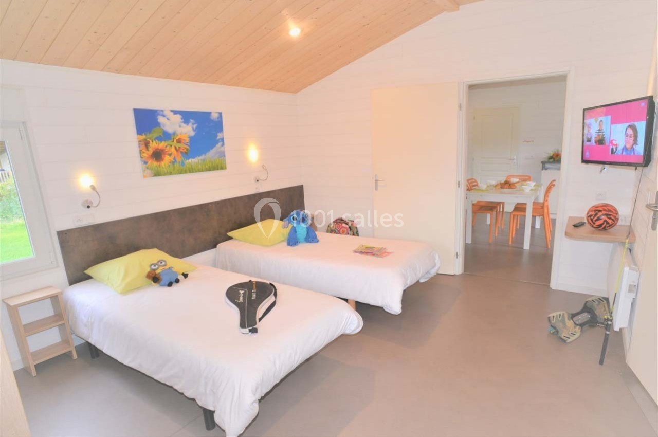 Location salle Merdrignac (Côtes-d'Armor) - Val de Landrouet #20 Chambre lumineuse avec deux lits simples, jouets posés dessus, et vue sur une table dans une pièce adjacente.