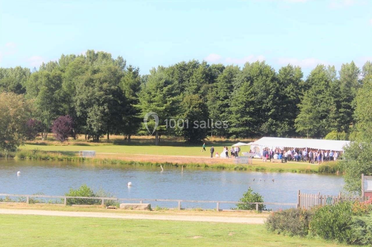Location salle Merdrignac (Côtes-d'Armor) - Val de Landrouet #7 Un étang entouré d'arbres avec une tente blanche accueillant un groupe de personnes sur la rive.